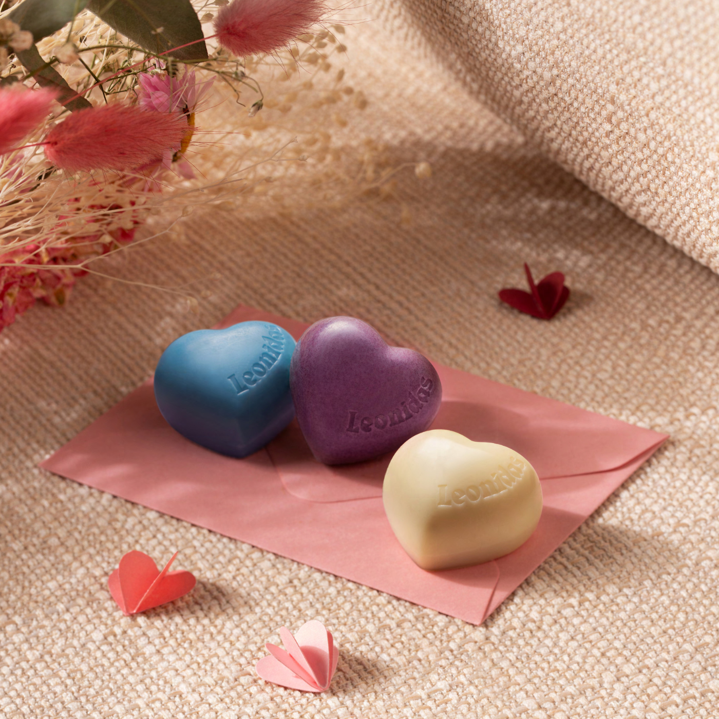 Heart-shaped chocolates on a pink envelope with dried flowers and fabric in the background